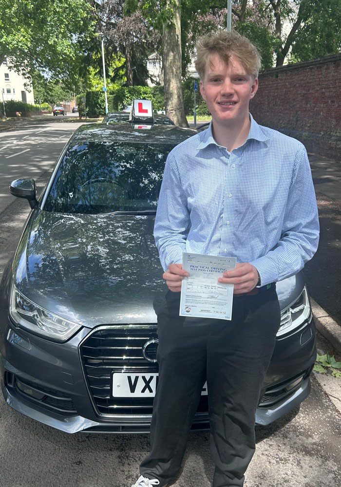 Learner holding a practical driving test pass certificate beside a tuition car