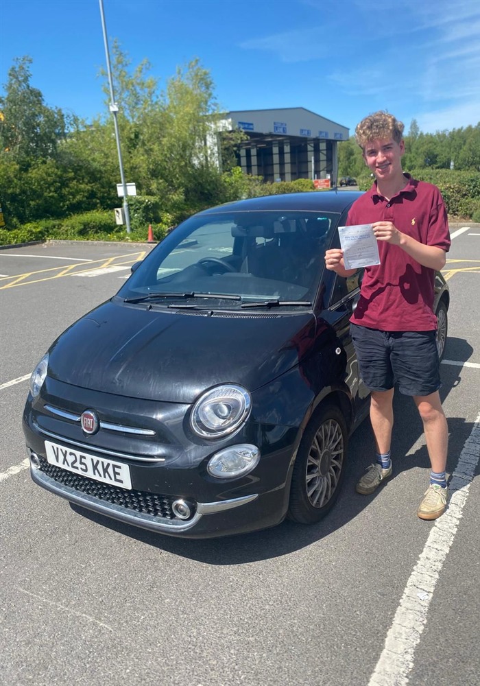 Learner holding a practical driving test pass certificate beside a car