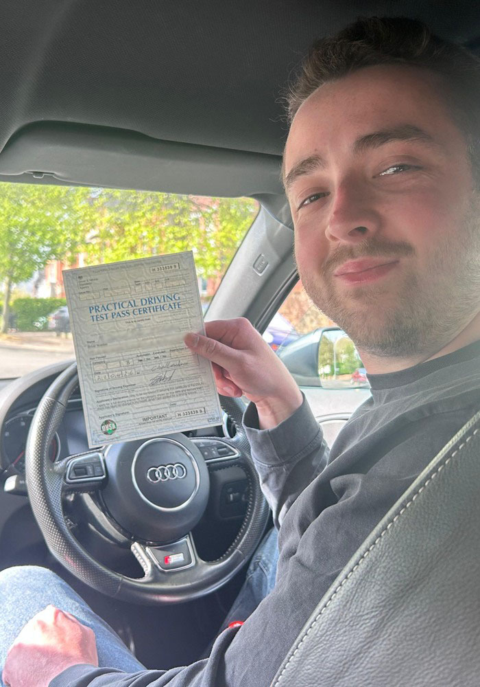 Learner holding a practical driving test pass certificate inside a tuition car