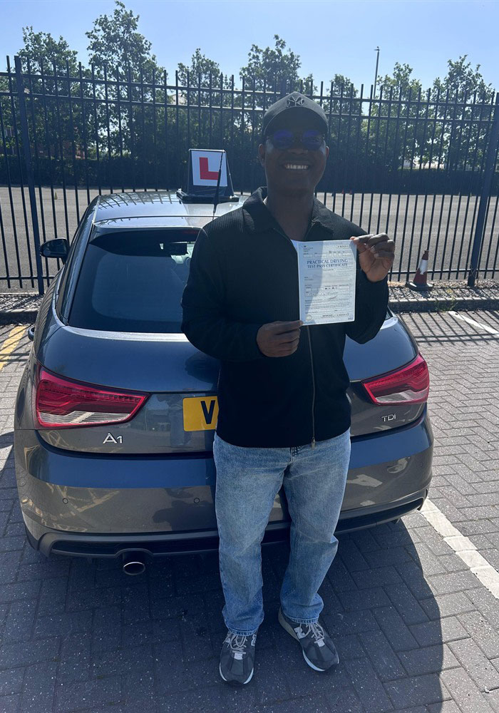 Learner holding a practical driving test pass certificate by a tuition car