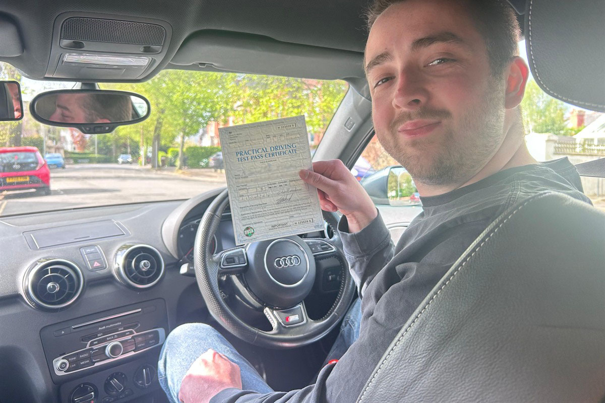 Learner holding a practical driving test pass certificate inside a tuition car